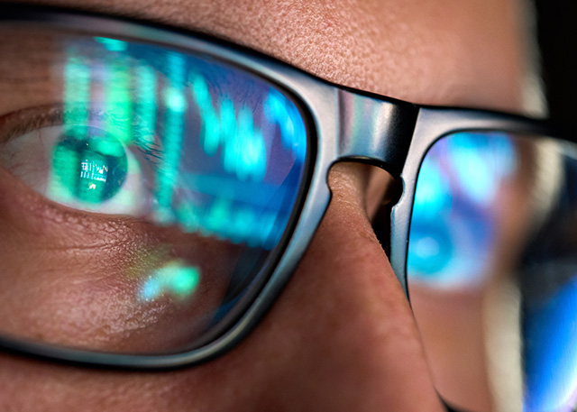 Close-up of a person's glasses reflecting computer code and data, symbolizing cybersecurity monitoring or coding.